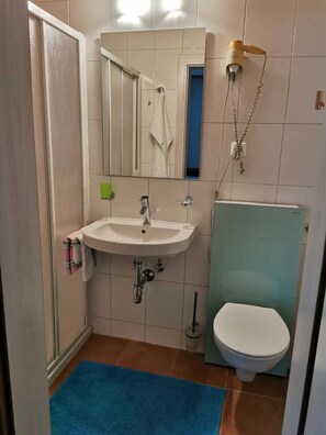 Un baño con lavamanos, espejo, toallero, inodoro y un secador de pelo montado en la pared.