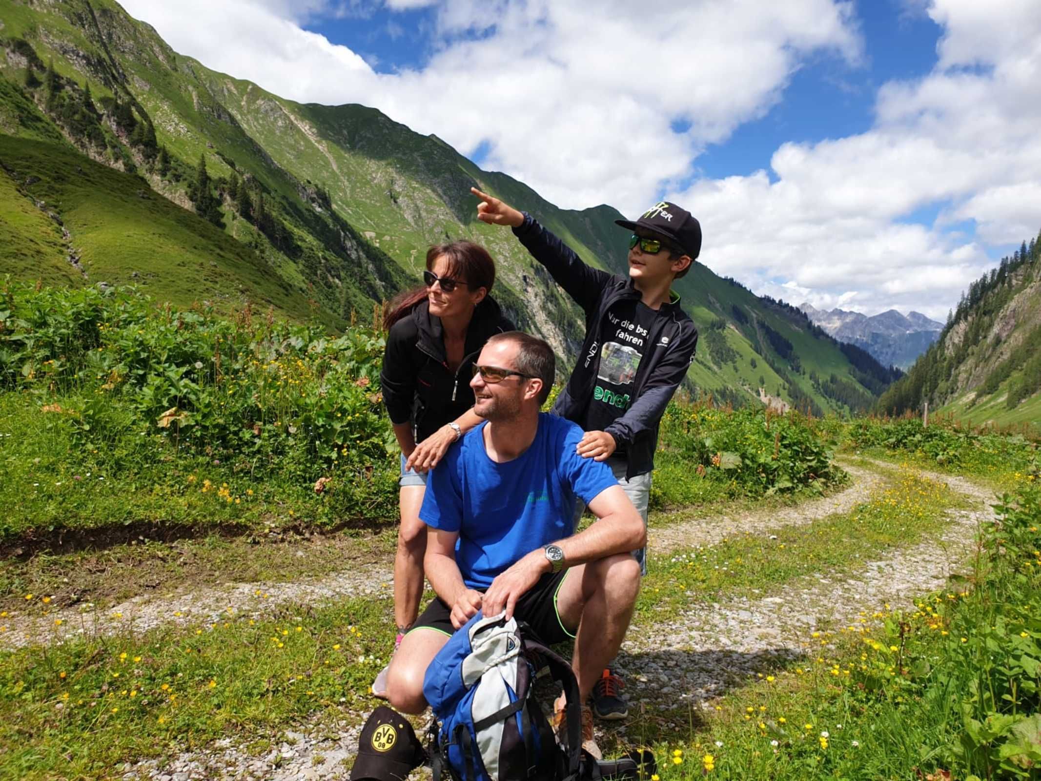 Eine Gruppe von Menschen auf einem Bergpfad, im Hintergrund viel Grün und Berge.