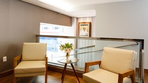 A balcony with two beige chairs, a small round table with a vase of flowers, and a framed picture on the wall.
