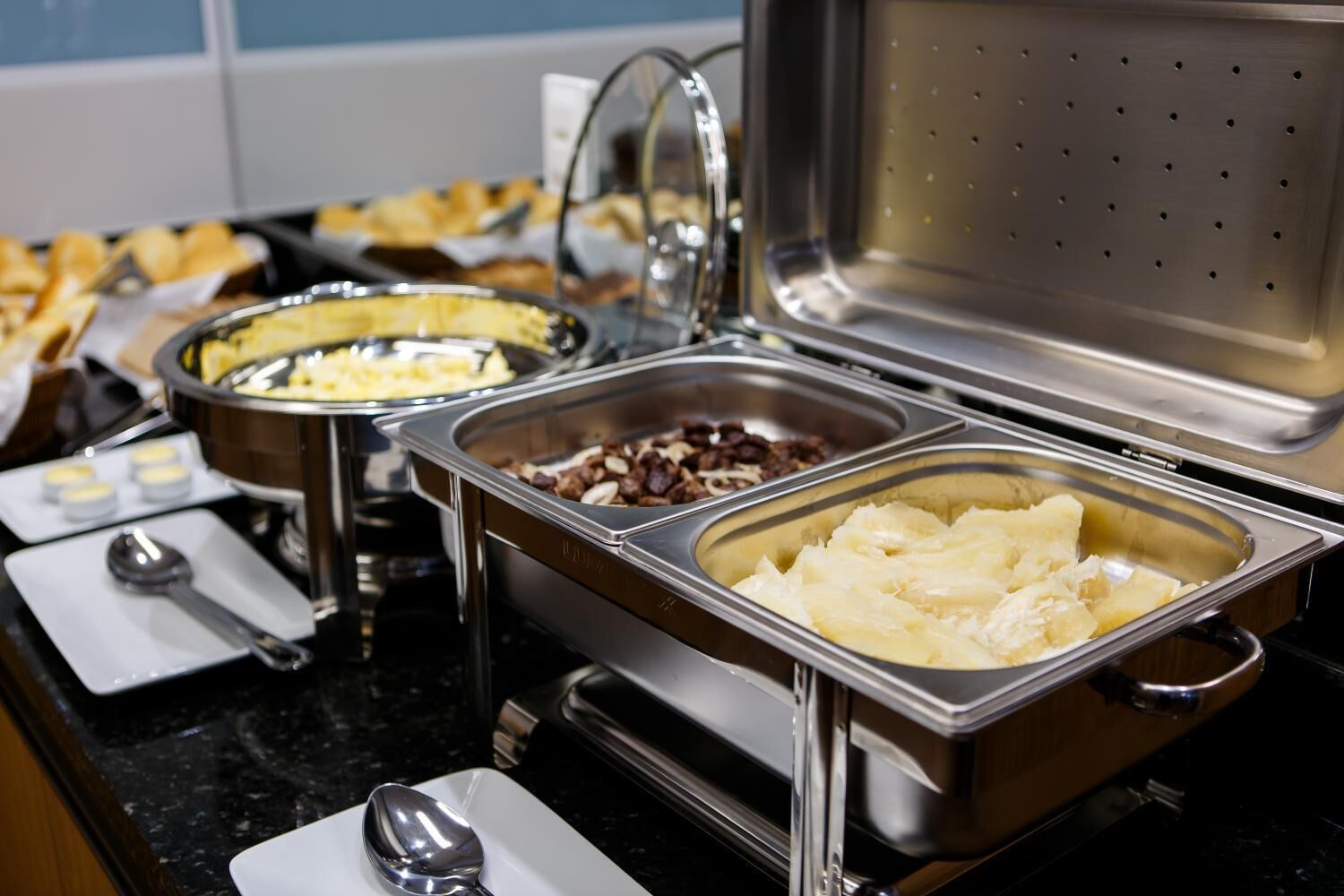 Una barra de buffet con distintos alimentos en recipientes de acero inoxidable.