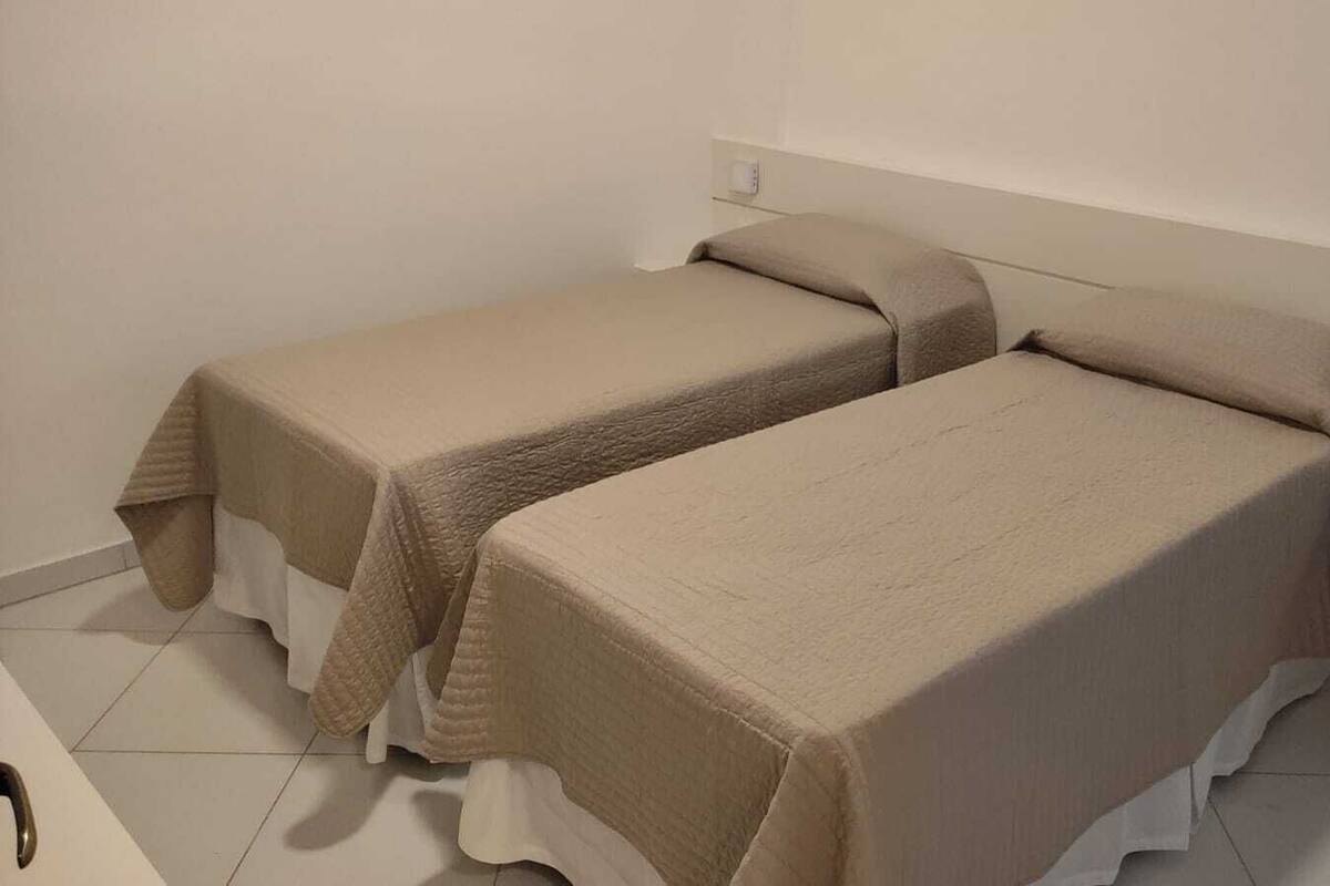Two single beds with beige bedding in a room with white walls and a small bedside table.
