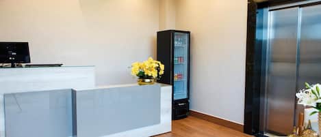 A reception area with a white reception desk, a black cabinet, a refrigerator, and an elevator.