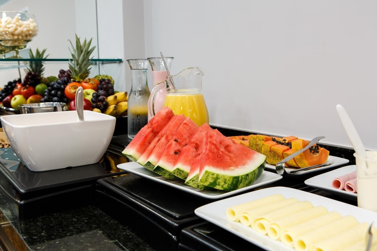 Un buffet della colazione con diversi tipi di frutta, un lavandino e una caraffa di succo.