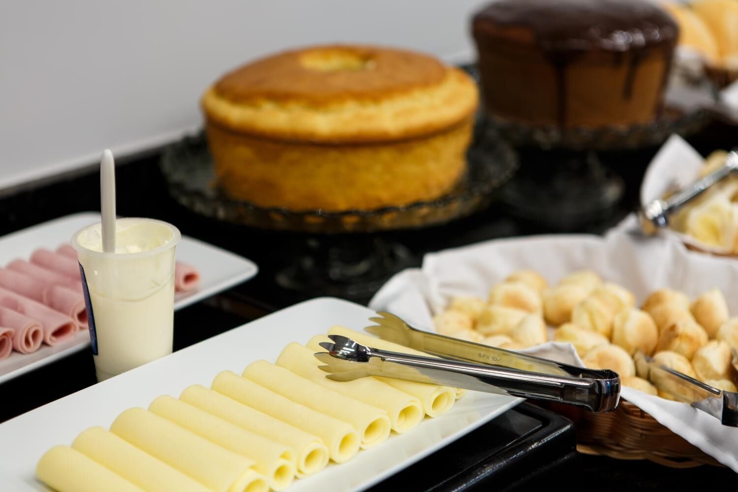 Buffet com diversas opções de comida, incluindo pães, um bolo e sobremesas.