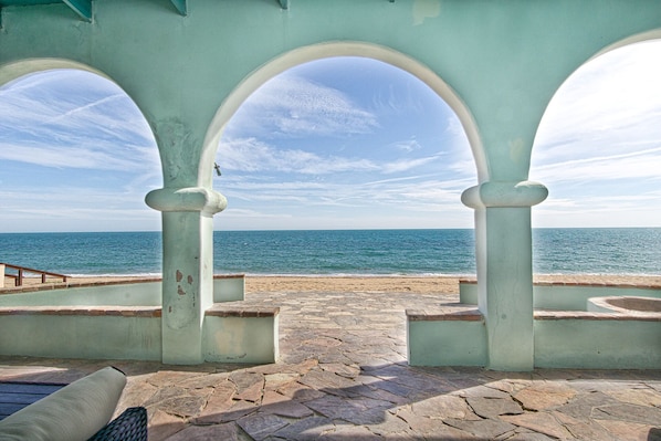 Une terrasse dallée de pierres, agrémentée d’arcades, qui offre une vue sur une plage et l’océan.