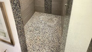 Eine Dusche mit gefliestem Boden und Wänden, einer Handbrause und einem vertikalen Ablaufrinnensieb.