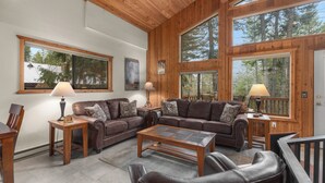 Ein gemütliches Wohnzimmer mit Holzwänden und großen Fenstern, ausgestattet mit Ledersofas und einem Couchtisch.