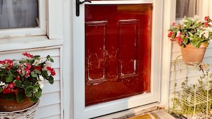Une porte rouge avec un panneau de verre, une pancarte de bienvenue au-dessus, et des plantes en pot de chaque côté.