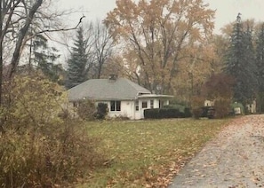 Uma casa térrea, cercada por árvores e um gramado.