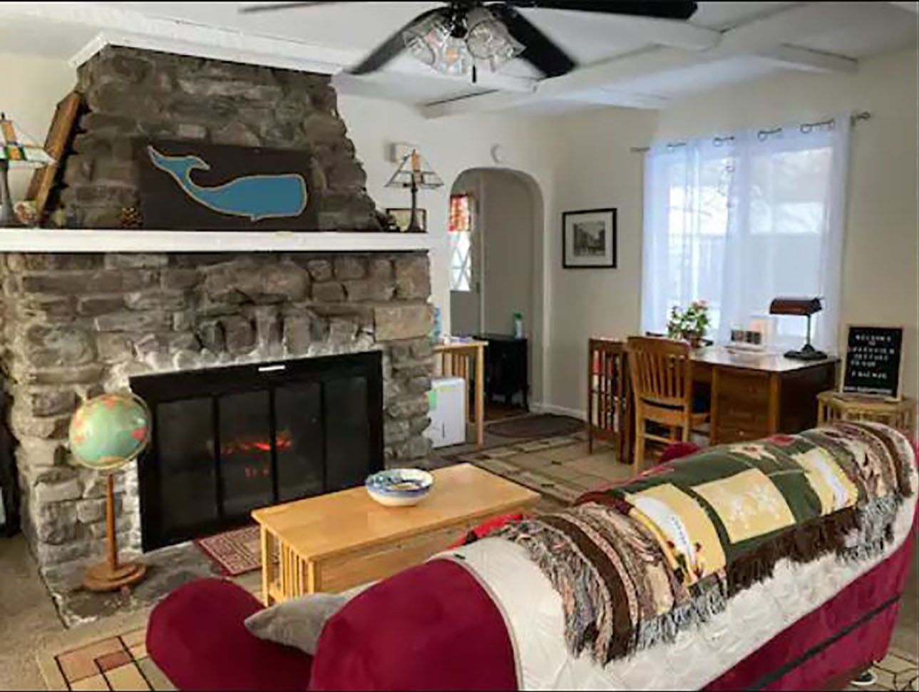 A cozy living room with a stone fireplace, a red sofa, a wooden coffee table, and a globe on a stand.