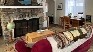 Un salon chaleureux avec une cheminée en pierre, un canapé rouge, une table basse en bois et un globe terrestre posé sur un pied.