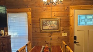 Une salle à manger en bois, ornée d’un lustre, avec un tableau encadré au mur et une table mise avec des bougies.