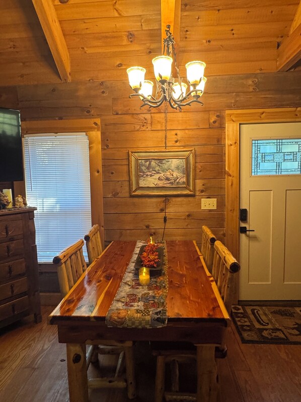 A wooden dining room with a chandelier, a framed picture on the wall, and a table set with candles. - BRAND NEW JACUZZI HOT TUB Real Log Cabin, Beautiful Rushing Trout Stream, Wifi. (Deep Gap)