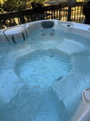 A hot tub with clear water and bubbles, surrounded by a wooden deck and chairs. - BRAND NEW JACUZZI HOT TUB Real Log Cabin, Beautiful Rushing Trout Stream, Wifi. (Deep Gap)
