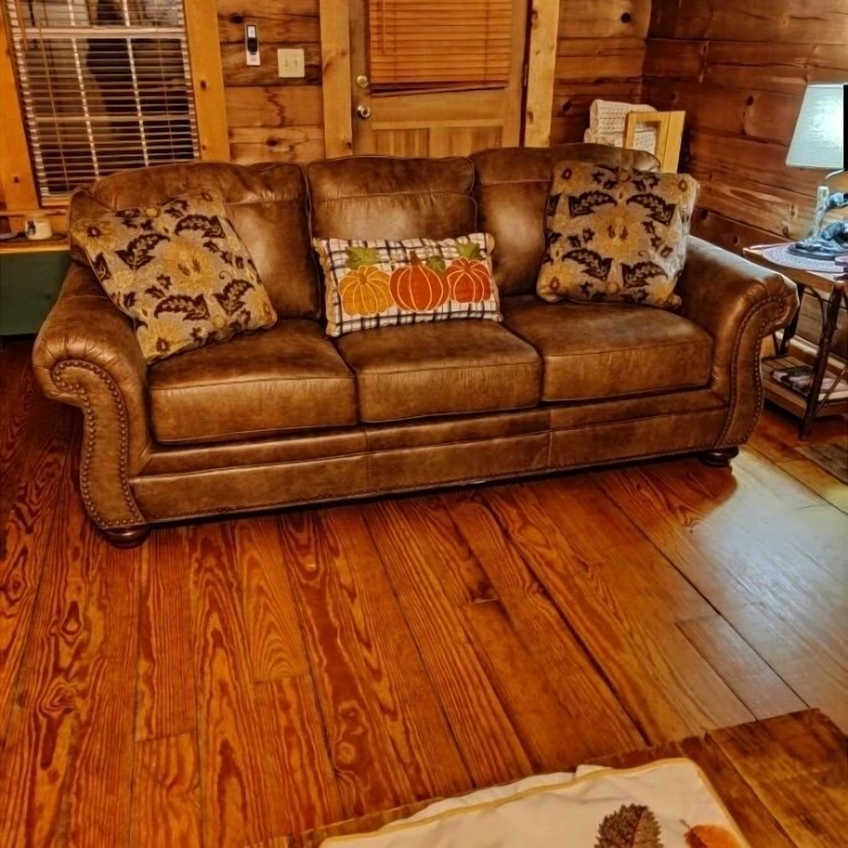 A brown leather sofa with patterned cushions, a wooden floor, and a wooden wall.