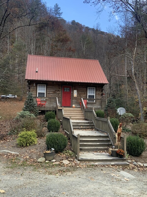 A rustic cabin with a red door, wooden stairs, and a satellite dish. - BRAND NEW JACUZZI HOT TUB Real Log Cabin, Beautiful Rushing Trout Stream, Wifi. (Deep Gap)