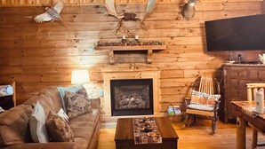 L’intérieur d’un chalet confortable, avec un plafond en bois, une cheminée, un canapé, un fauteuil et une table.