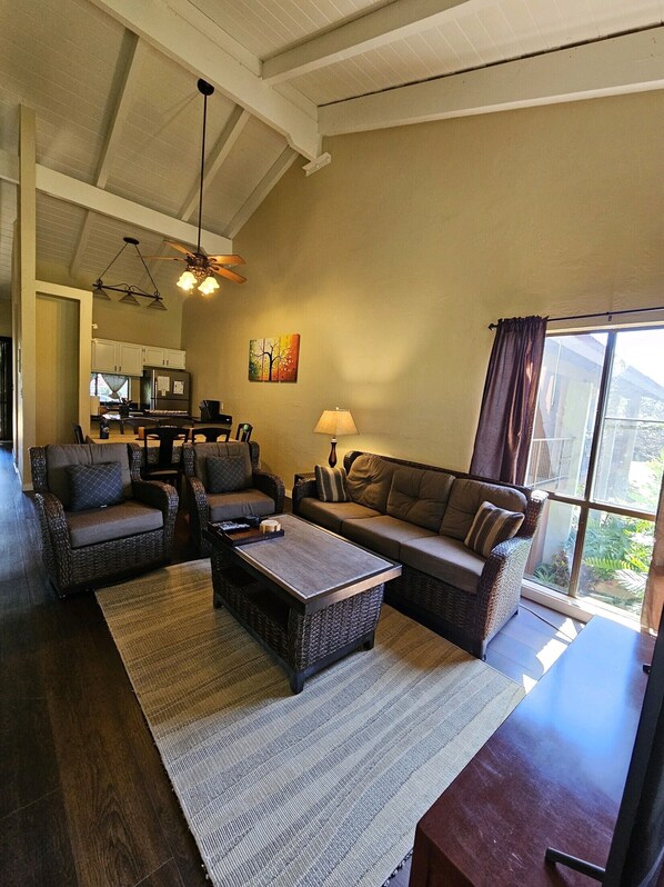 A spacious living room with wicker furniture, a dining table, and a kitchen in the background.
