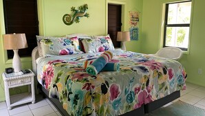 Une chambre à coucher avec une couvre-lit à motifs floraux, deux lampes de chevet, une décoration murale et une fenêtre donnant sur un beau paysage.