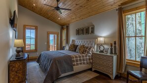 A bedroom with a large bed, wooden ceiling, and a view of the outdoors.