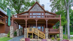 A two-story log cabin with a stone foundation, wooden deck, and a stone chimney.