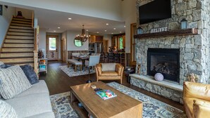 A spacious living area with a stone fireplace, a wooden staircase, and a dining area.
