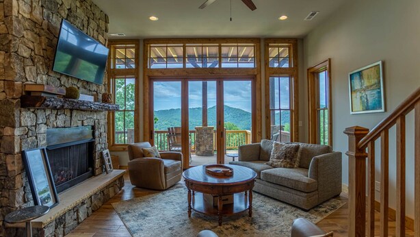 A spacious living room with a stone fireplace, comfortable seating, and large windows offering a view of the outdoors.