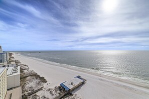 Un hotel frente a la playa con un muelle largo que se adentra en el océano, una playa de arena y un cielo despejado.