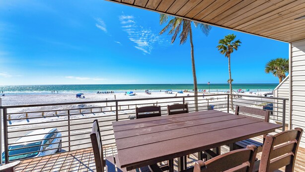 A beachside patio with a wooden table and chairs, overlooking a sandy beach with palm trees and the ocean. - Breathtaking 4 Bedroom/ 4 Bath Town Home Located Directly on Siesta Key Beach! (Siesta Key)