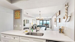 A modern kitchen with a large island, stainless steel sink, and white cabinetry. There is a view of the ocean through large windows. - Breathtaking 4 Bedroom/ 4 Bath Town Home Located Directly on Siesta Key Beach! (Siesta Key)