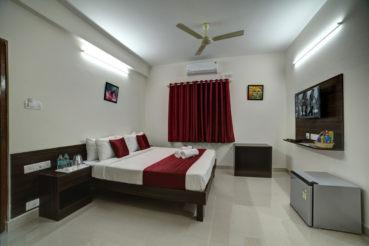 A hotel room with a bed, a nightstand, a TV, a ceiling fan, and a small refrigerator.