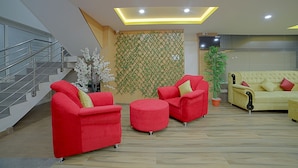 Un área de estar moderna con una escalera, sofás rojos y amarillos, y una planta grande en maceta.