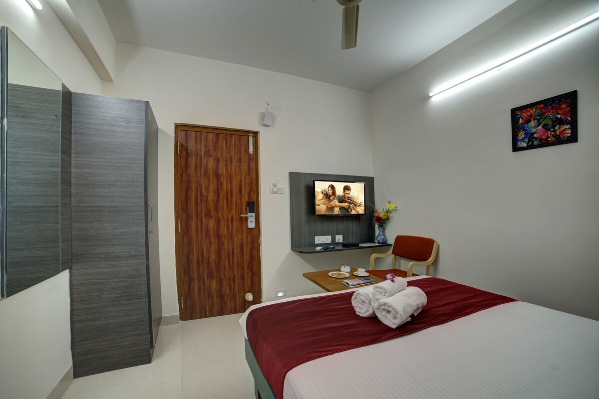 A hotel room with a bed, a TV, a desk, and a chair.