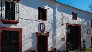 Ein weißes Gebäude mit roten Fensterrahmen und -türen, einem kleinen Balkon und einem dekorativen Metallstück über der Tür.