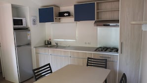Eine kleine Küche mit Mikrowelle, Kühlschrank, Spüle und einem kleinen Gaskochfeld. Über der Arbeitsfläche befinden sich Schränke und ein Tisch mit Stühlen.