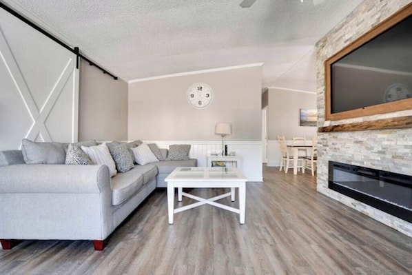 A living room with a sofa, coffee table, fireplace, and a clock on the wall. - Shore to Please. Big family, pet friendly beach house. (North Cape May)