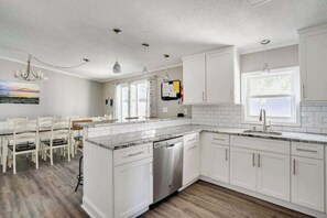 A modern kitchen with white cabinetry, a dishwasher, and a dining area with a table and chairs.