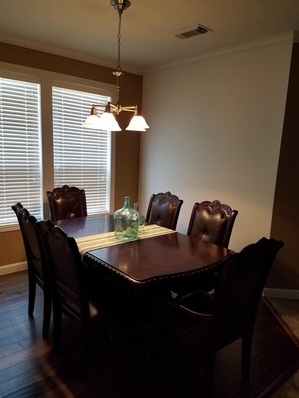 A dining room with a wooden table and chairs, a chandelier, and windows with blinds.