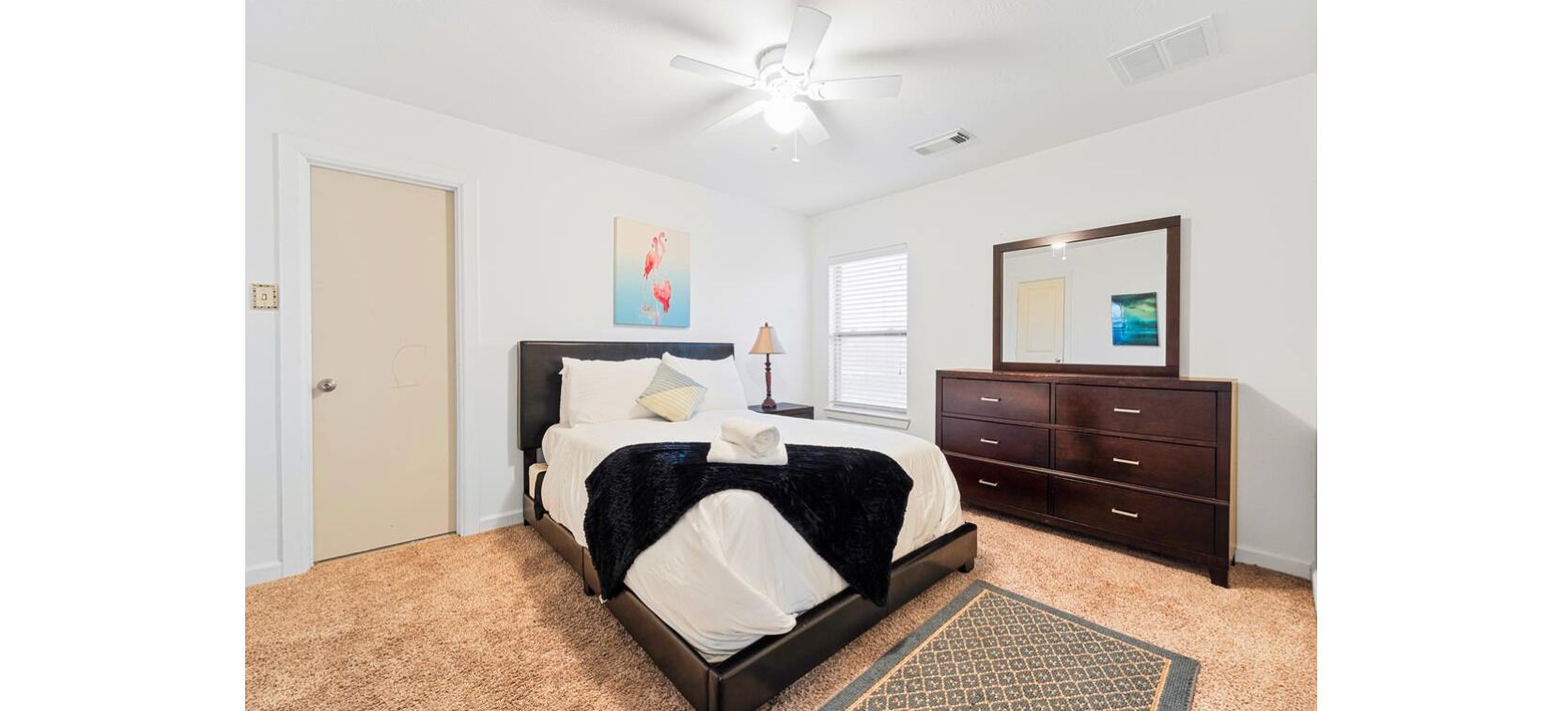A bedroom with a bed, a dresser, a mirror, and a ceiling fan.