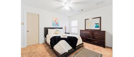 A bedroom with a bed, a dresser, a mirror, and a ceiling fan.