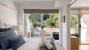 Een slaapkamer met een bed, kussens, een nachtkastje met een lamp, en uitzicht op een terras met stoelen en een tafel.