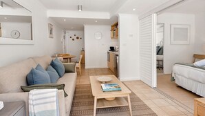 Een moderne, goed verlichte woonkamer met een bank, salontafel en uitzicht op de keuken en slaapkamer.