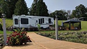 En træbro fører hen til en hvid autocamper ved navn 'Sandpiper', med et overdækket siddeområde og en lille pavillon.