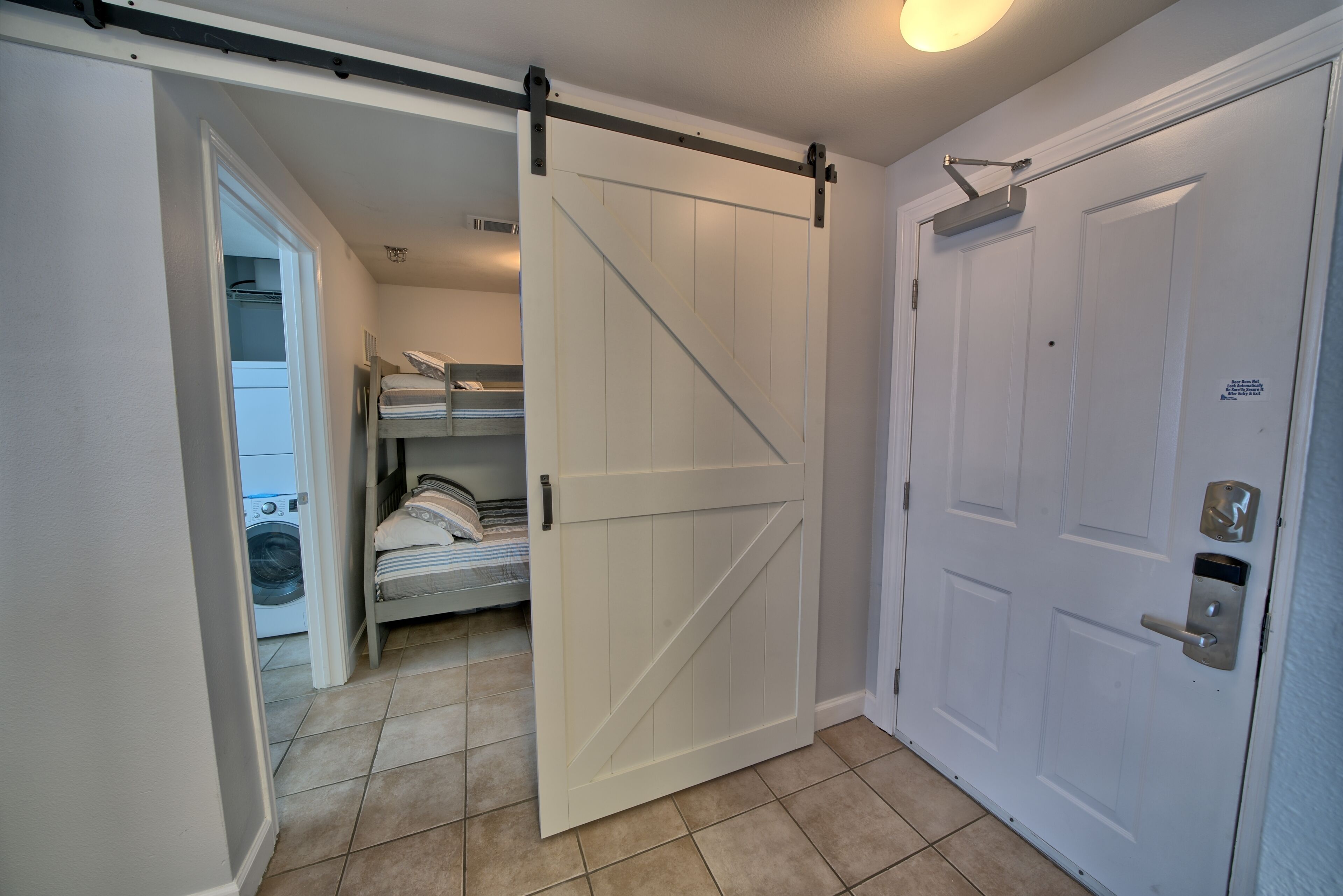 A bedroom with a sliding door, a bed, a washing machine, and a closet.