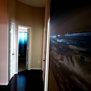 Stunning hallway with a glimpse into a bathroom featuring a large painting and a blue shower curtain.