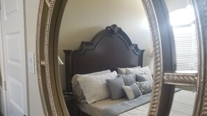 Une chambre à coucher avec un grand miroir décoratif, une tête de lit en bois foncé et un lit bien fait, agrémenté de plusieurs coussins.
