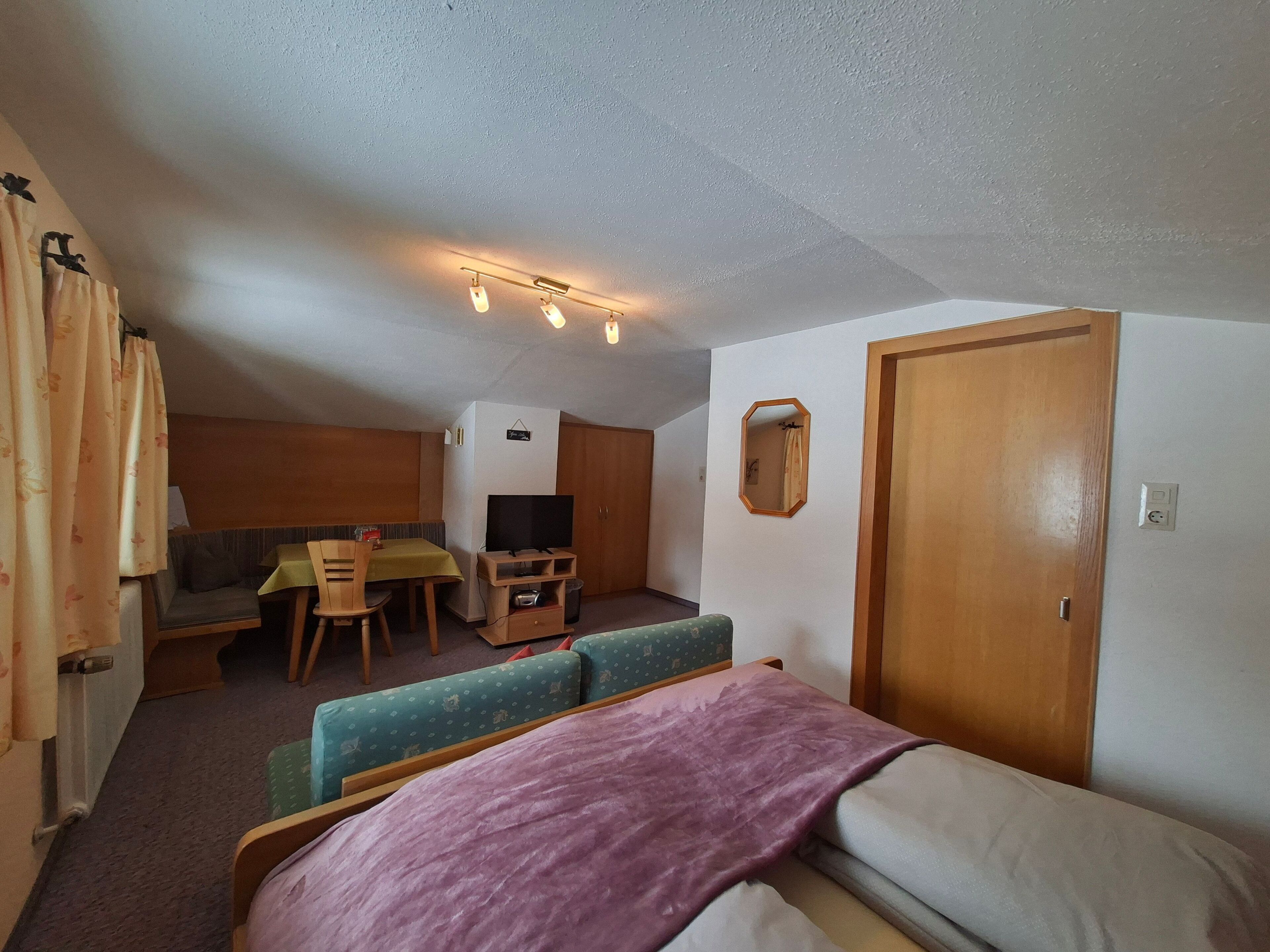 Una habitación compacta con cama, sofá, una mesita, televisor y puerta.