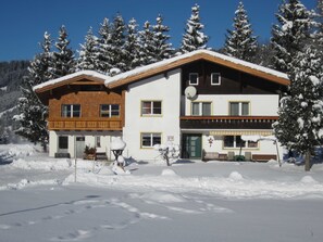 Een gebouw met twee verdiepingen, een houten balkon, een schotelantenne en een besneeerd landschap.