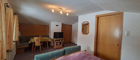 Una habitación compacta con cama, sofá, una mesita, televisor y puerta.