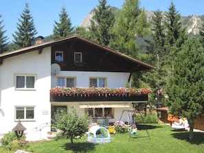 Un bâtiment à deux étages doté d’un balcon, entouré de verdure et de montagnes.